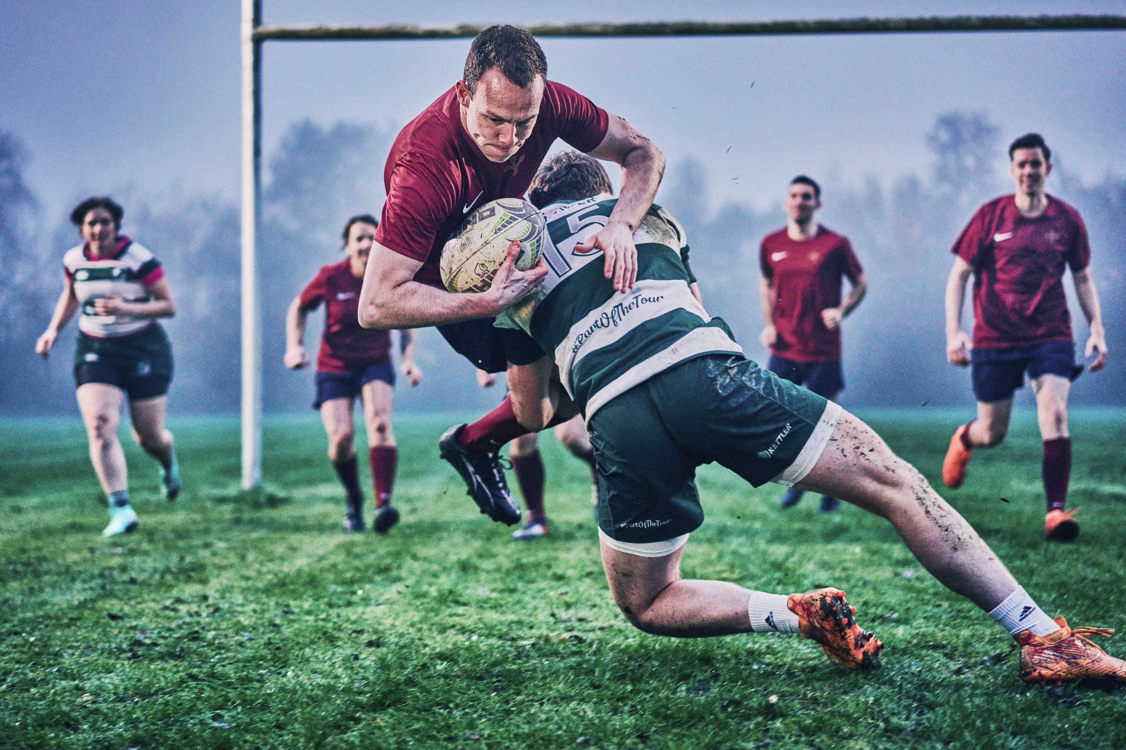 A HADLEY team player in a rugby match is tackled by an opponent, while teammates run in the background.